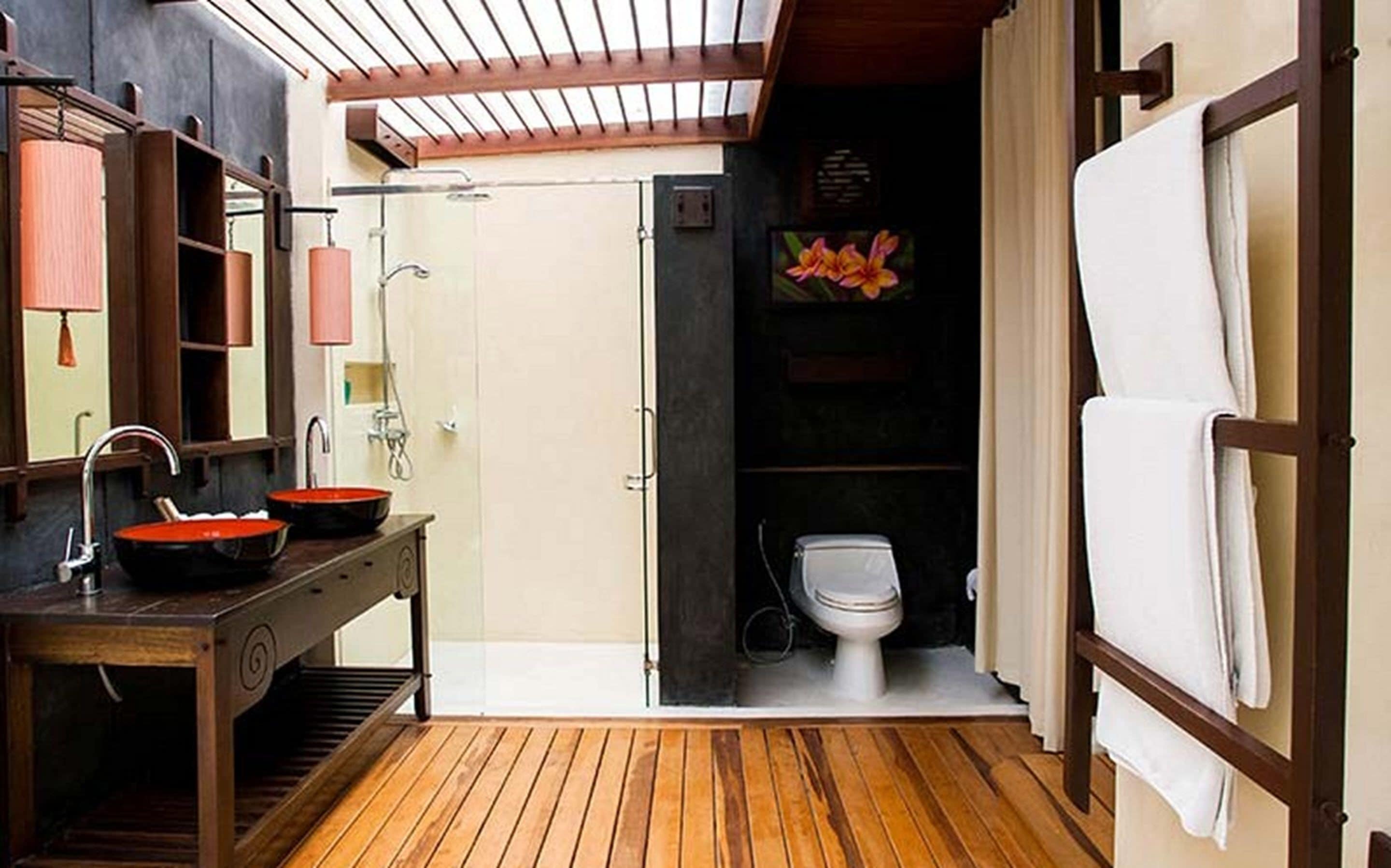 Une salle de bain au sol en bois, équipée d’un lavabo, d’un miroir et d’une douche.