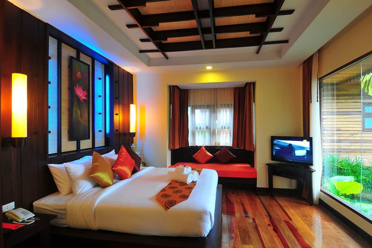 A hotel room with a large bed, a television, and a window with a view of greenery.