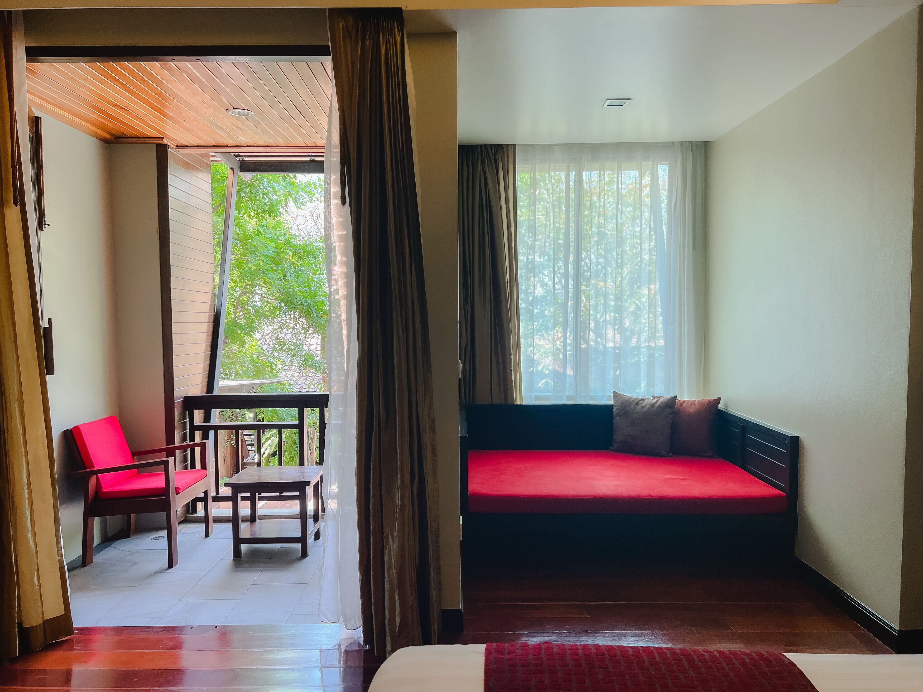 A room with a bed, a red sofa, a wooden table, and a red chair.