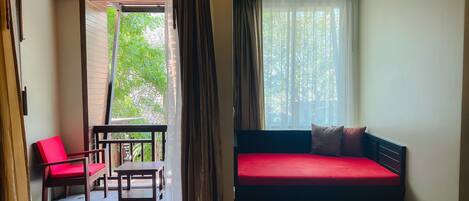 A room with a bed, a red sofa, a wooden table, and a red chair.