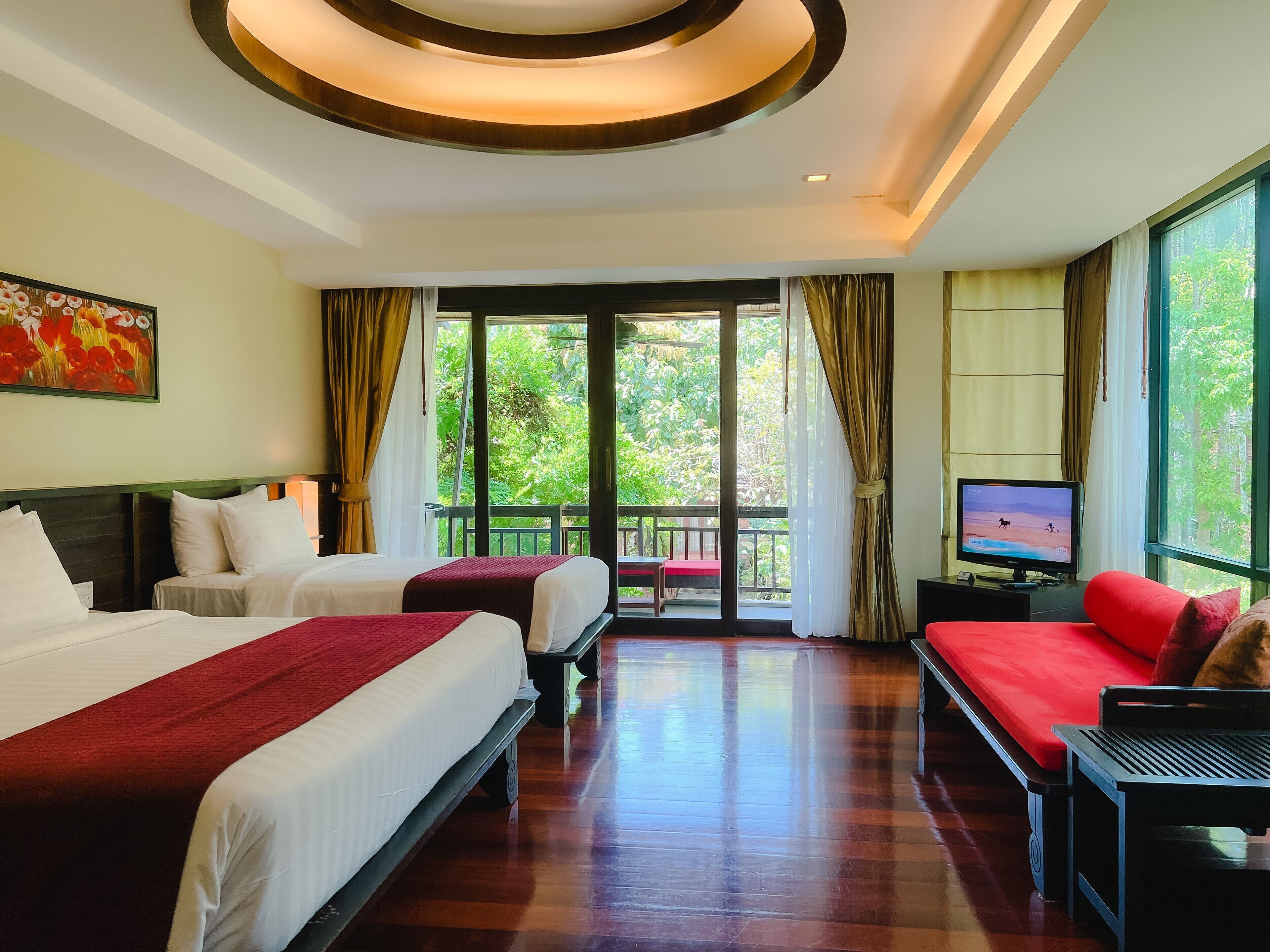 Habitación de hotel con dos camas, televisión y balcón con vistas a la vegetación.