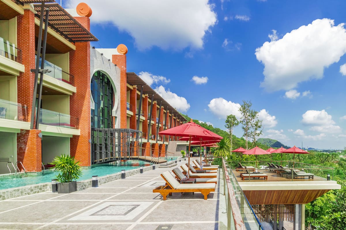 A hotel with a rooftop pool, red umbrellas, and lounge chairs.