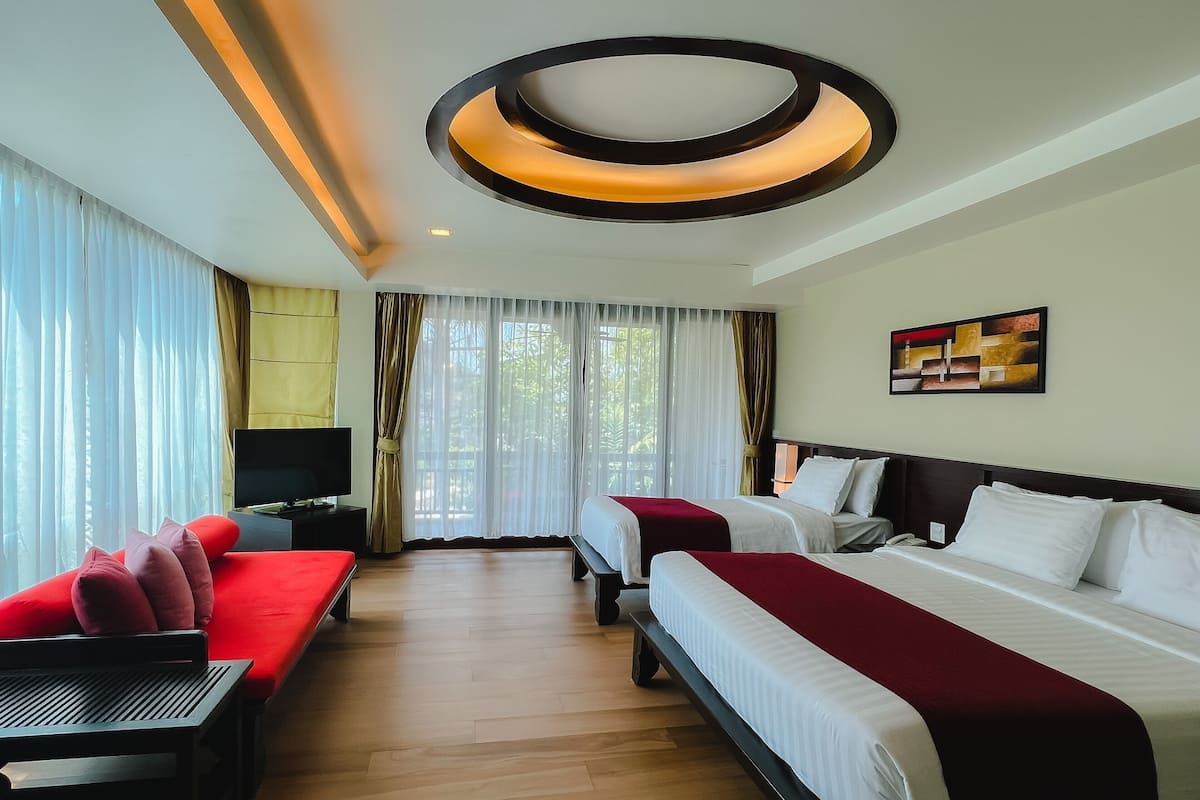 A hotel room with two beds, a TV, a sofa, and a large window with curtains.