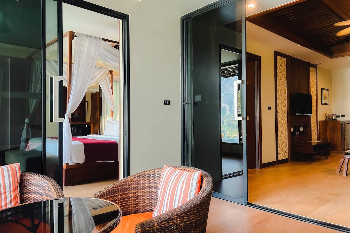A hotel room with a bed, a glass partition, a wicker chair, and a television.