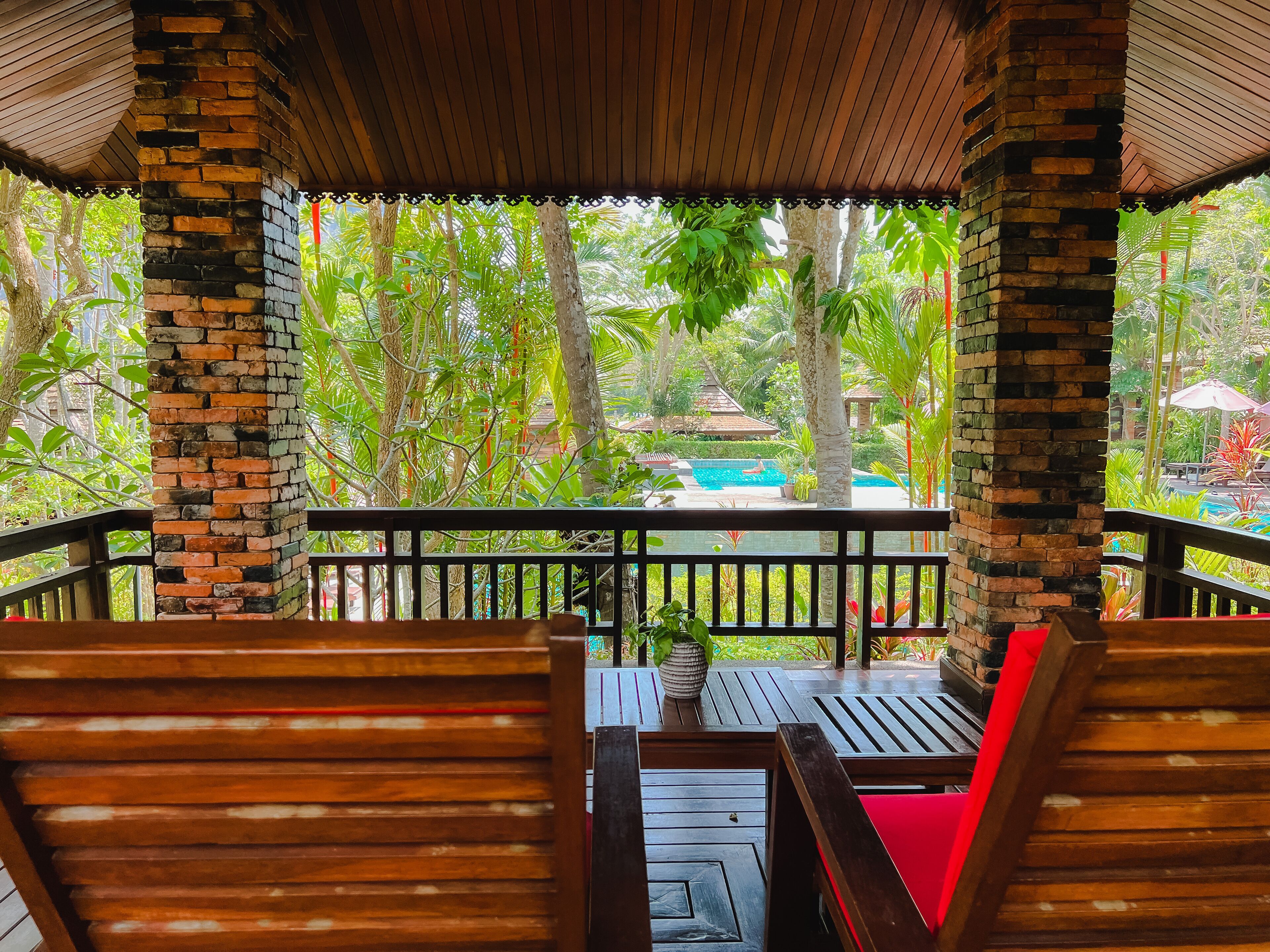 Terraza de madera con vista a la piscina, rodeada de exuberante vegetación.