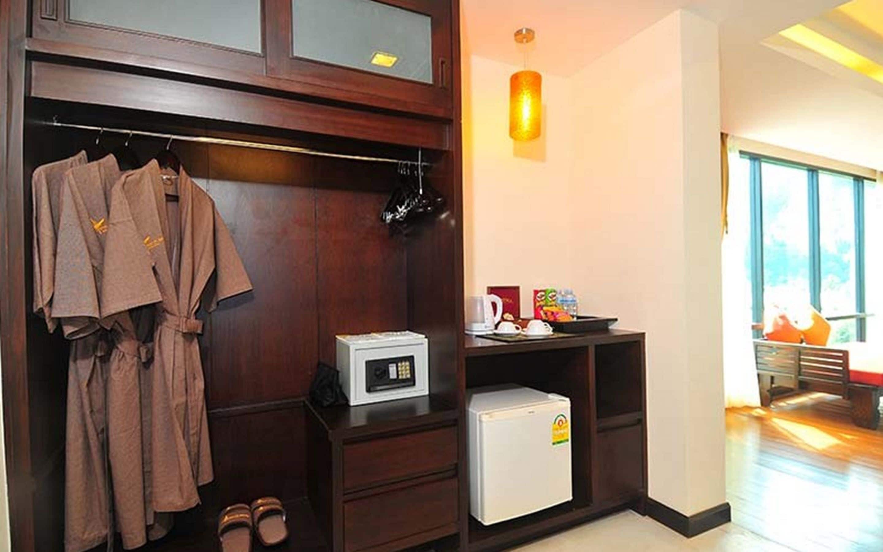 Habitación de hotel con armario de madera, microondas, refrigerador pequeño y zona de estar con mesa y sillas.