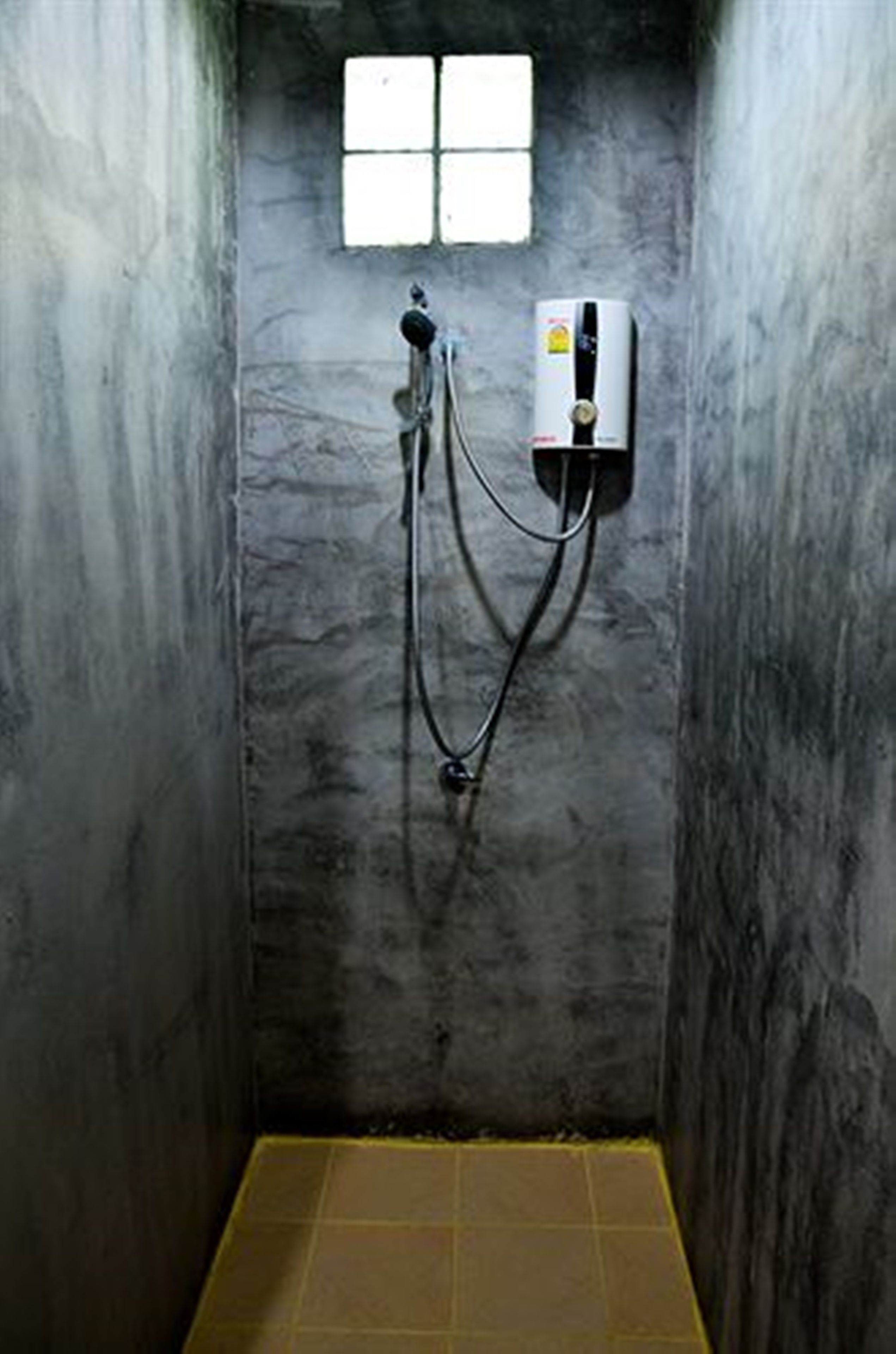 A small, enclosed shower area with a window, a water heater, and a tiled floor.