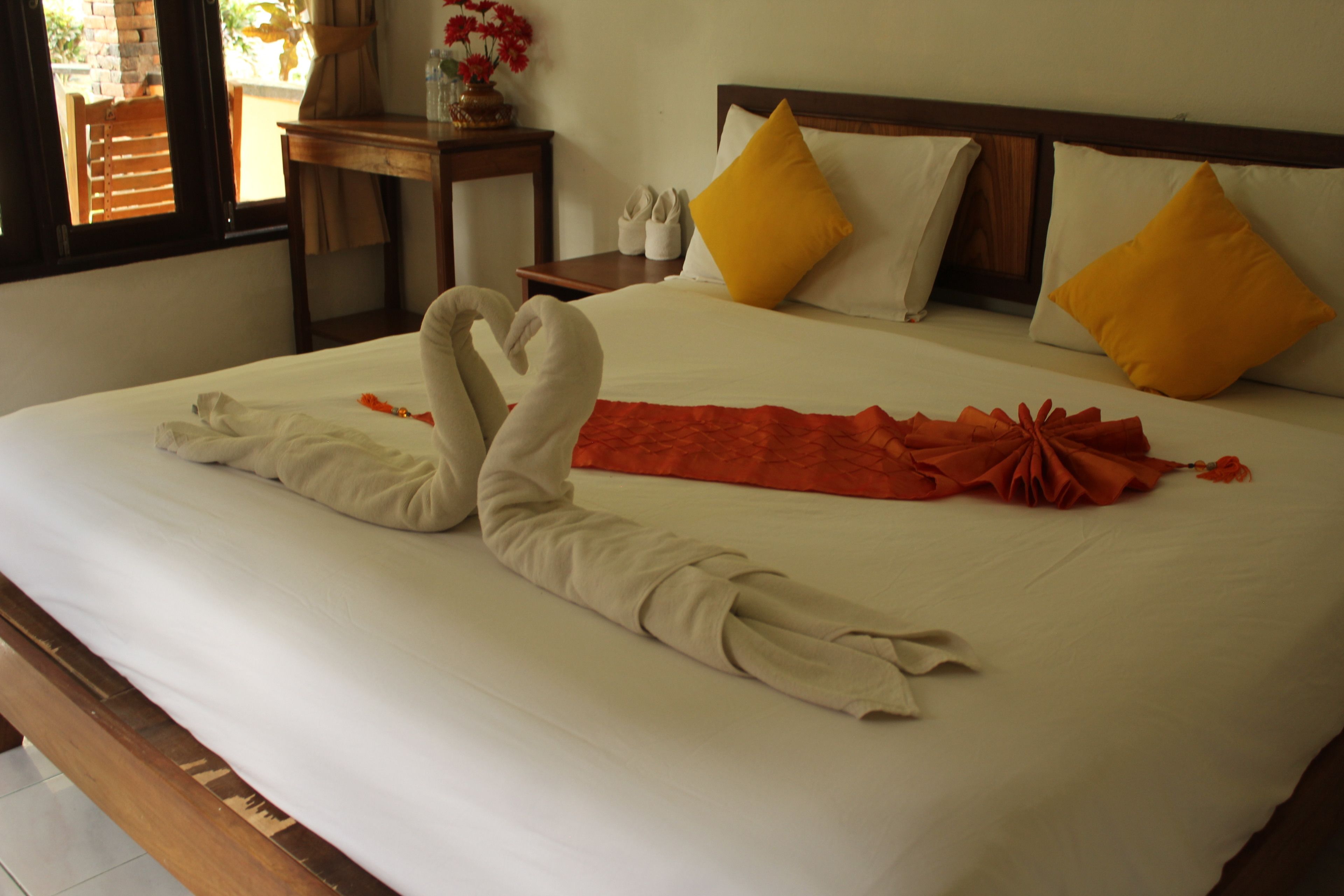 A neatly made bed with a swan towel design and a red cloth centerpiece.