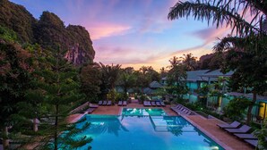 Una piscina rodeada de sillas de descanso y palmeras, con vistas a una montaña al fondo.