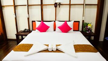 Una cama bien hecha con almohadas blancas y rosadas, una almohada decorativa marrón y una disposición de toallas en el centro.