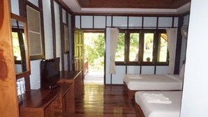 Una habitación con piso de madera, una cama, un televisor y un ventanal con cortinas.