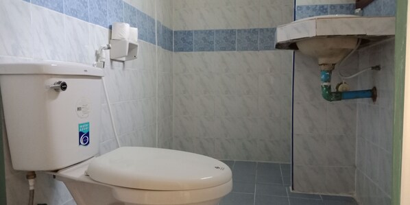 Une salle de bain équipée de toilettes, d’une étiquette indiquant qu’elles sont économes en eau et d’un porte-rouleau de papier toilette.