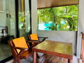 A wooden table and two chairs with orange cushions in a room with a view of lush green foliage through a window.
