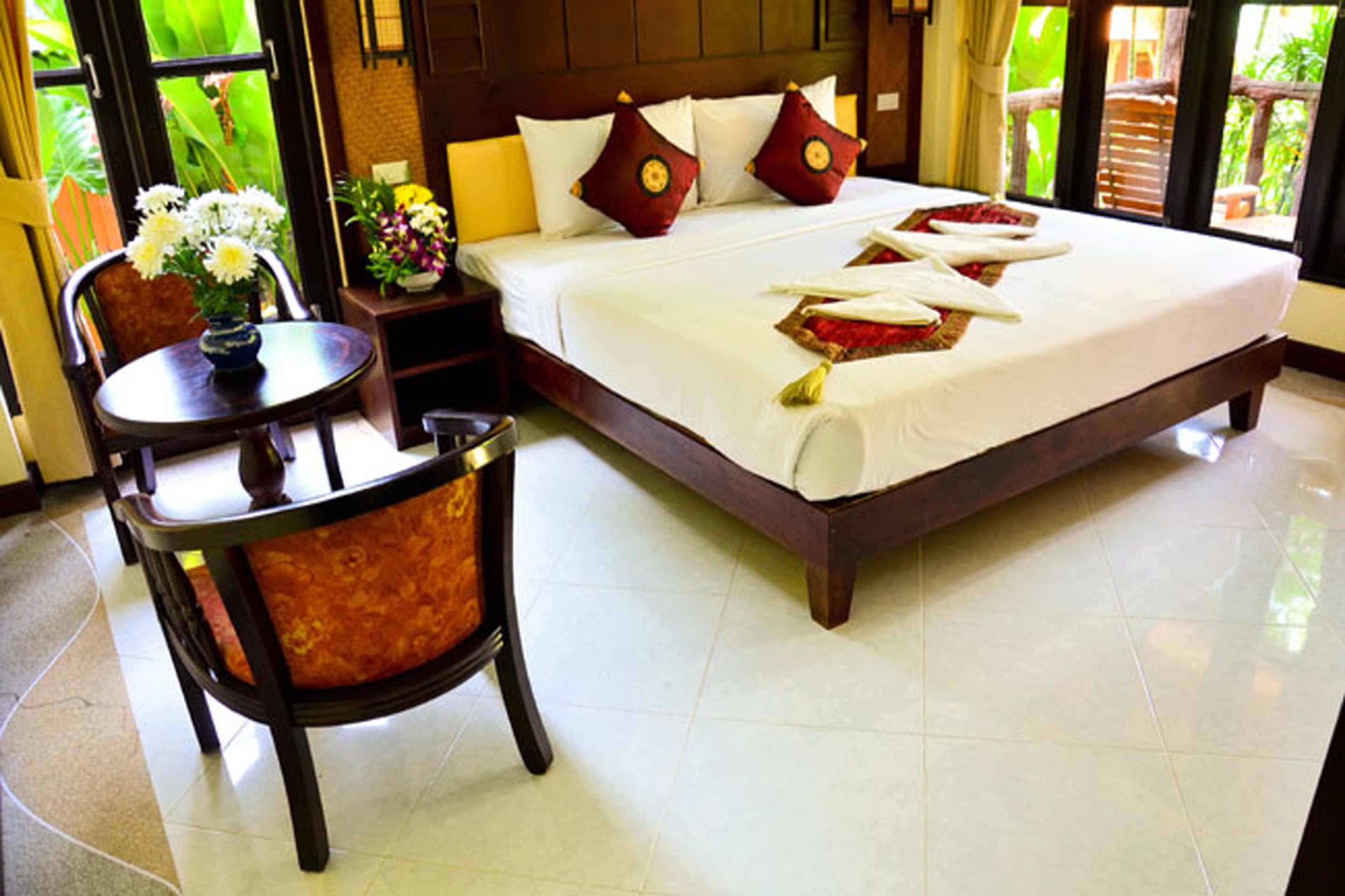 Une chambre d’hôtel avec un grand lit, une petite table ronde ornée d’un vase de fleurs et une chaise avec un coussin.
