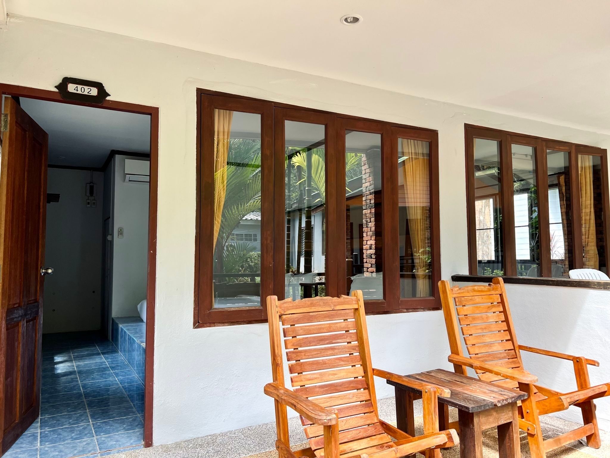 A room with two wooden chairs, a small table, and a view through large windows.