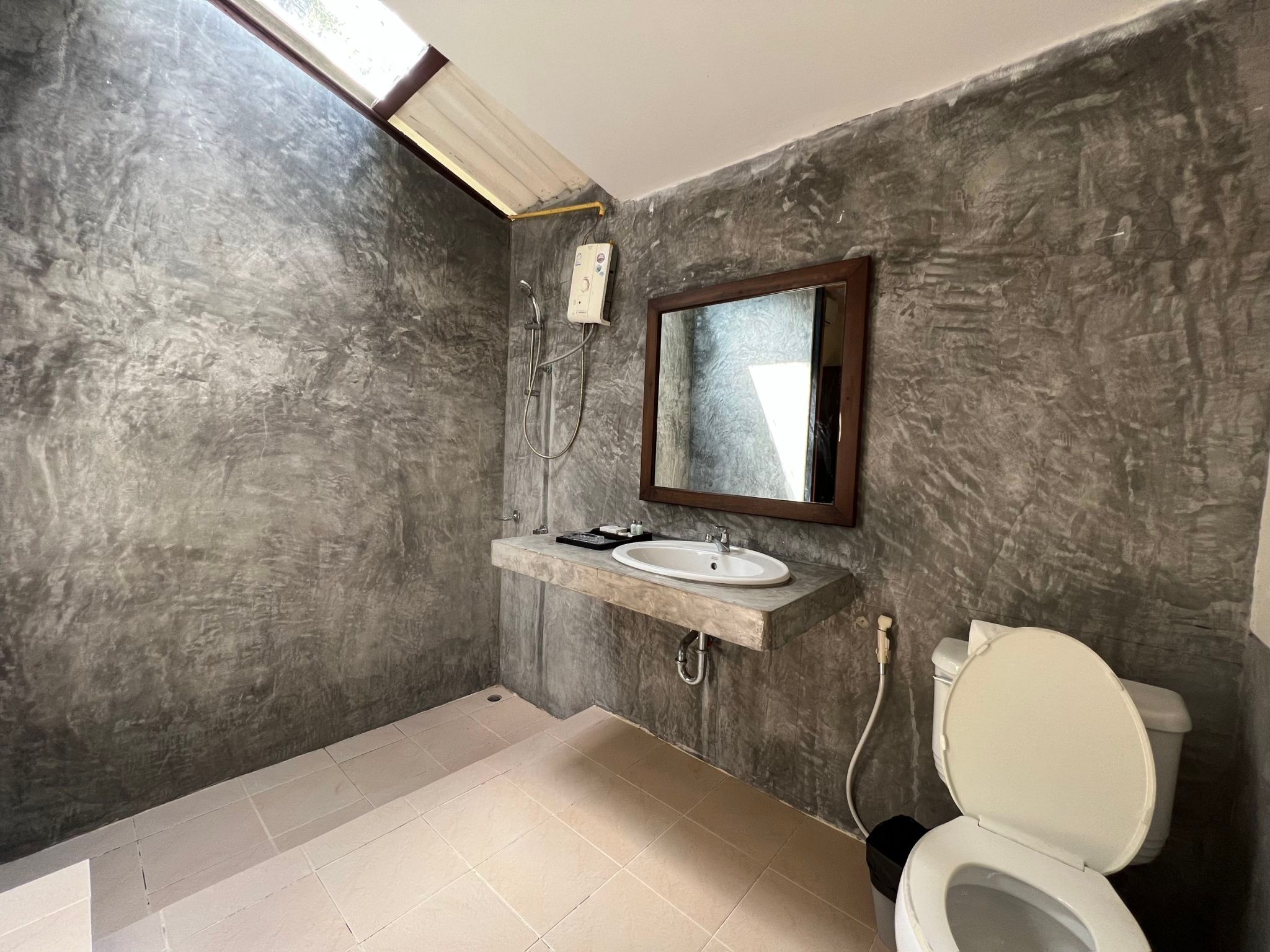 A bathroom with a marble wall, a sink with a mirror, a toilet, and a shower.