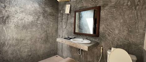 A bathroom with a marble wall, a sink with a mirror, a toilet, and a shower.