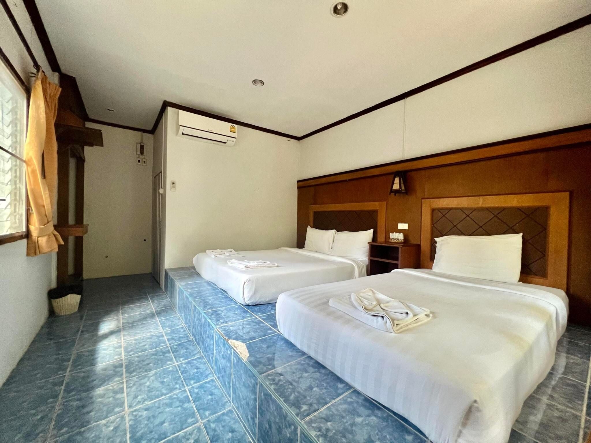 Une chambre d’hôtel avec deux lits, une fenêtre avec des rideaux, un climatiseur fixé au mur et un sol carrelé.