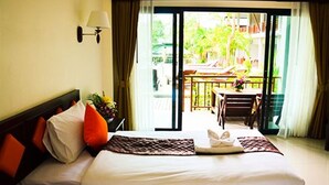 Habitación de hotel con cama, mesita de noche, lámpara, ventana con cortinas y vista al balcón exterior.