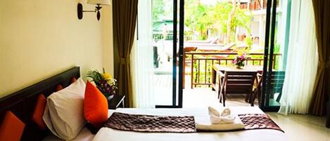 A hotel room with a bed, a nightstand, a lamp, a window with curtains, and a view of the outside balcony.