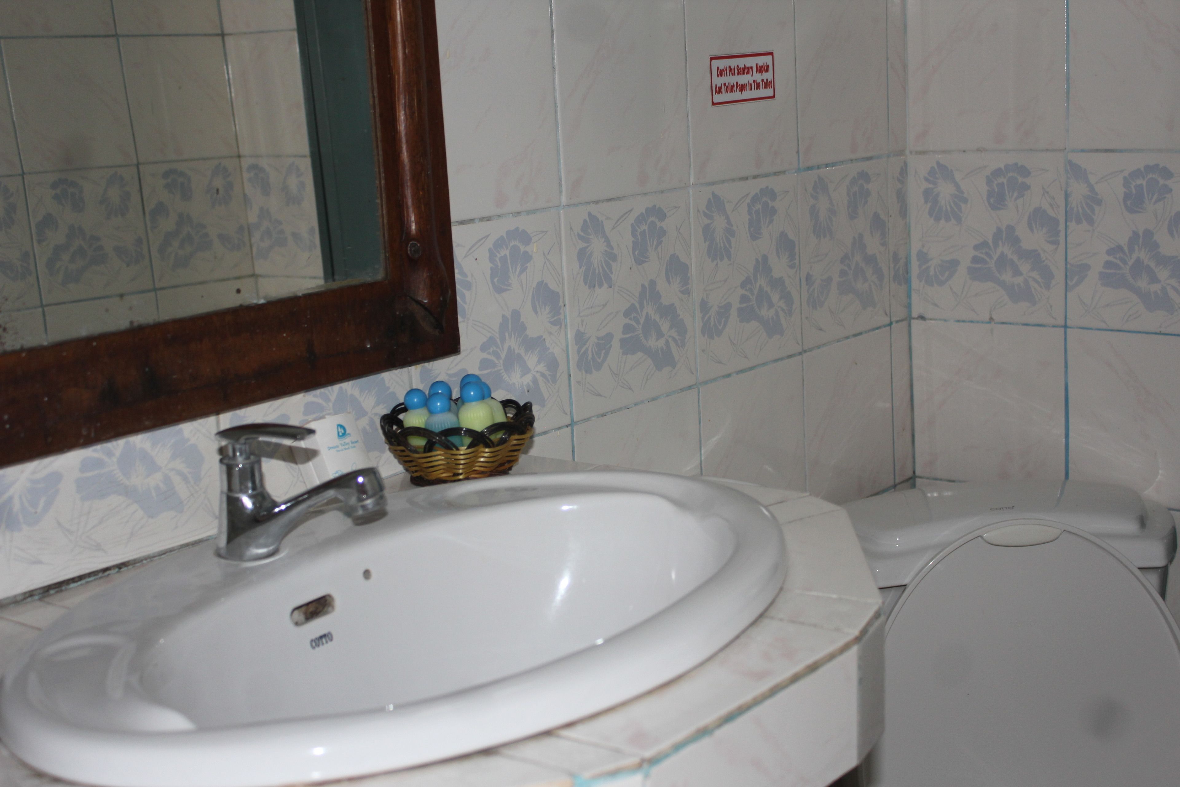 A bathroom with a white sink, a mirror, and a toilet. There is a basket of toiletries on the sink.