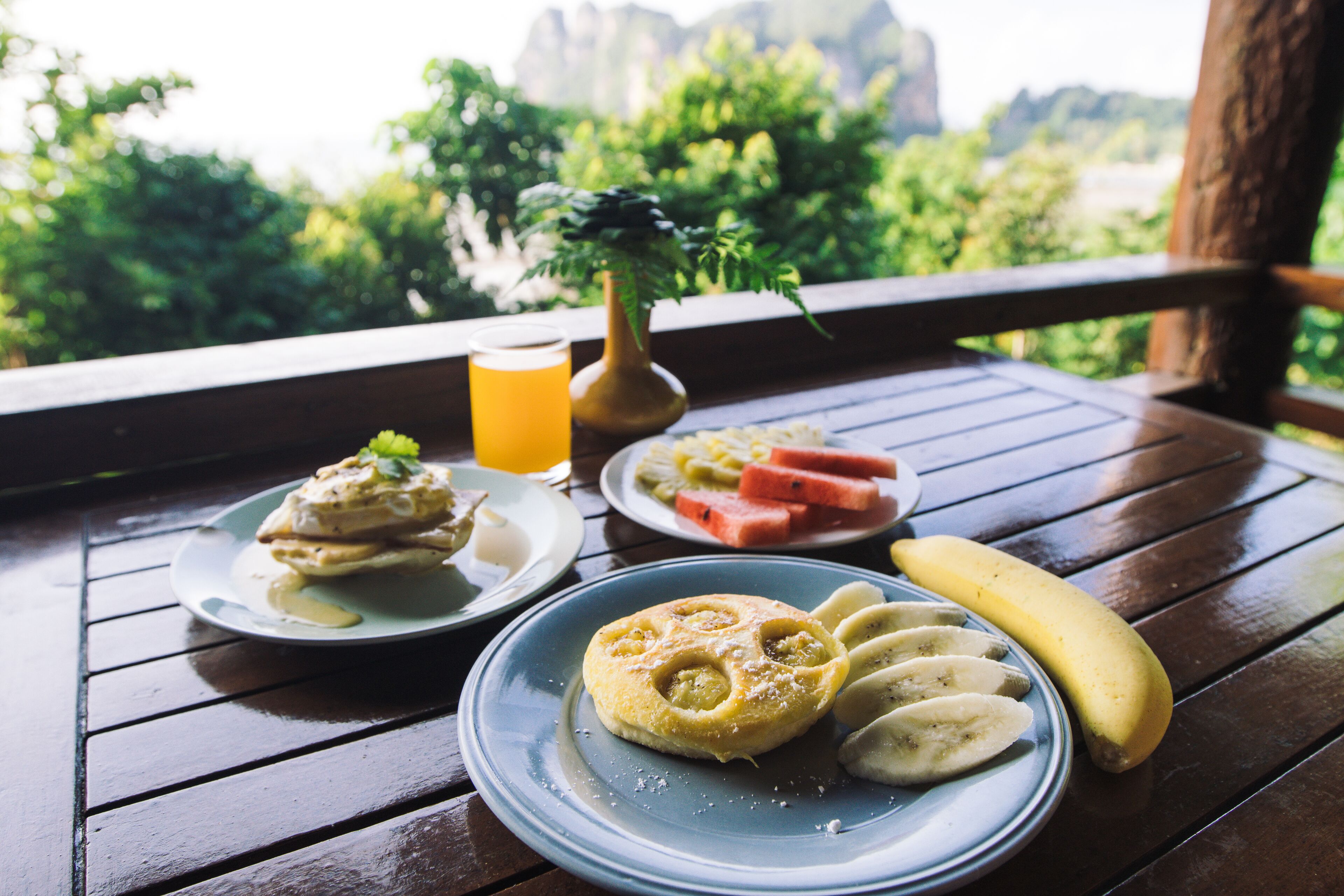 A wooden table with plates of food, a banana, and a glass of orange juice.