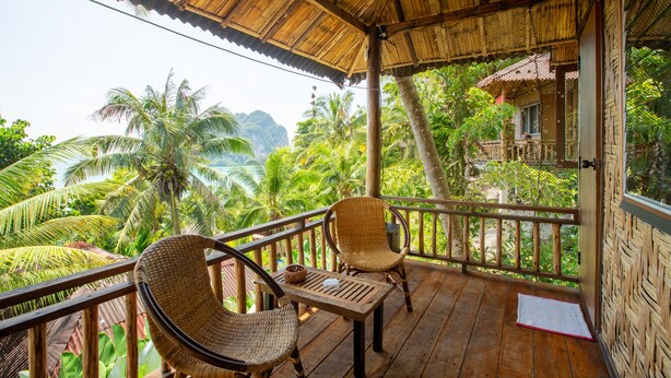 A wooden deck with wicker chairs and a table, overlooking a lush tropical landscape with palm trees and a mountain in the distance. - Railay Garden View Resort (Krabi)