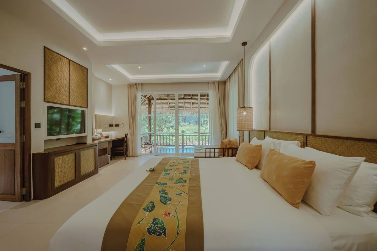 Habitación de hotel con una cama grande, un escritorio, televisión y un balcón con vistas a zonas verdes.