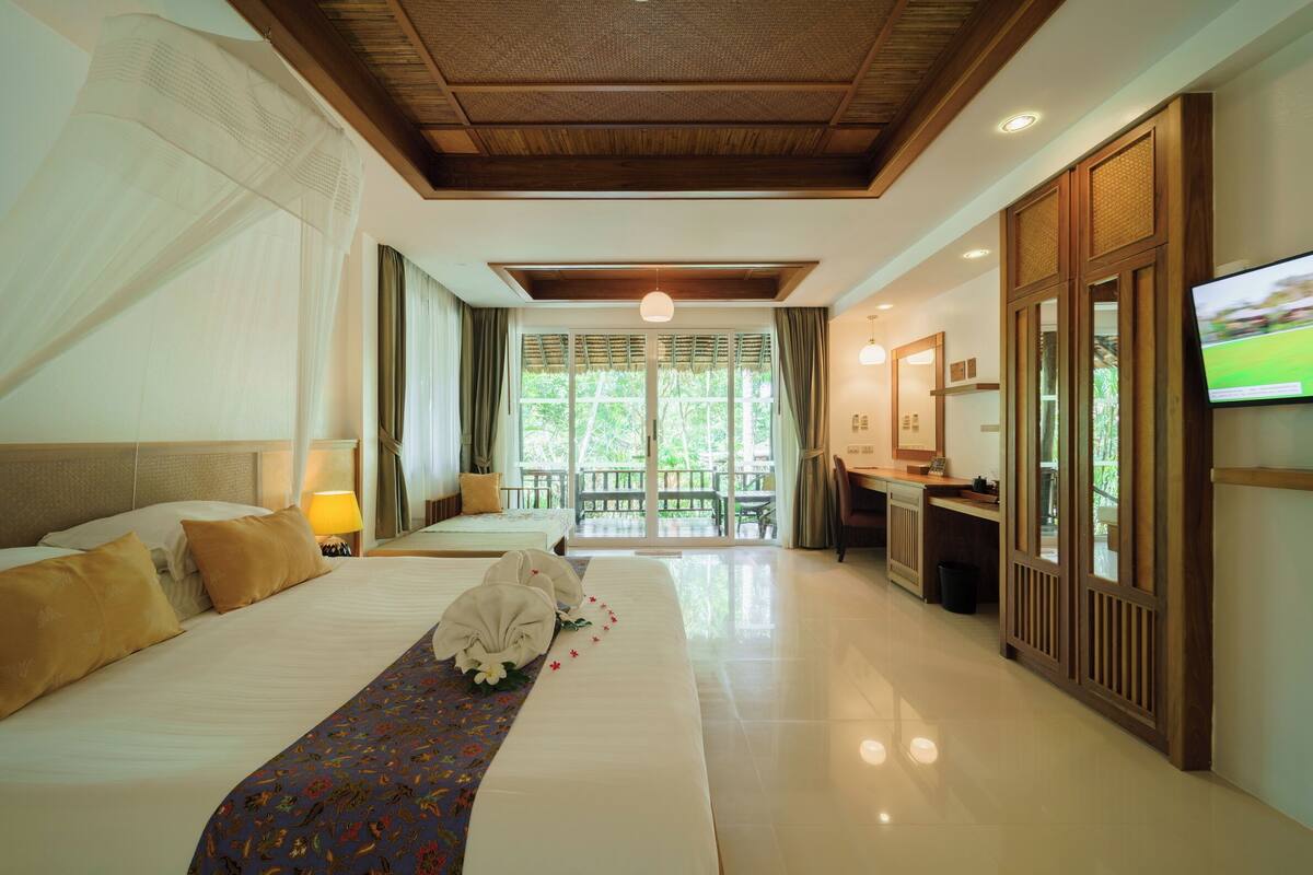 Habitación de hotel con una cama grande, un escritorio, un televisor y un balcón con vistas a zonas verdes.