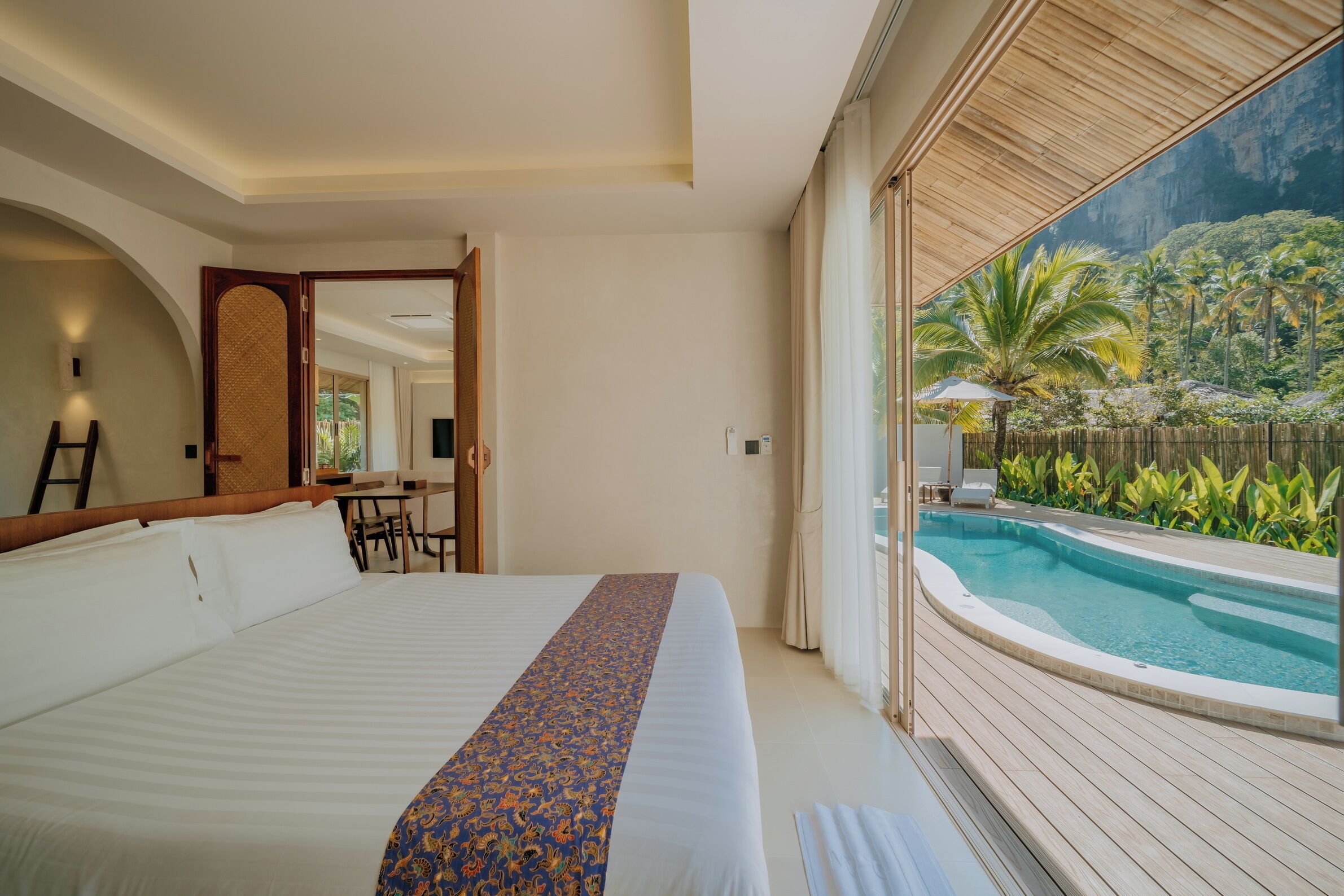 A hotel room with a large bed, a desk, and a view of a swimming pool with palm trees.