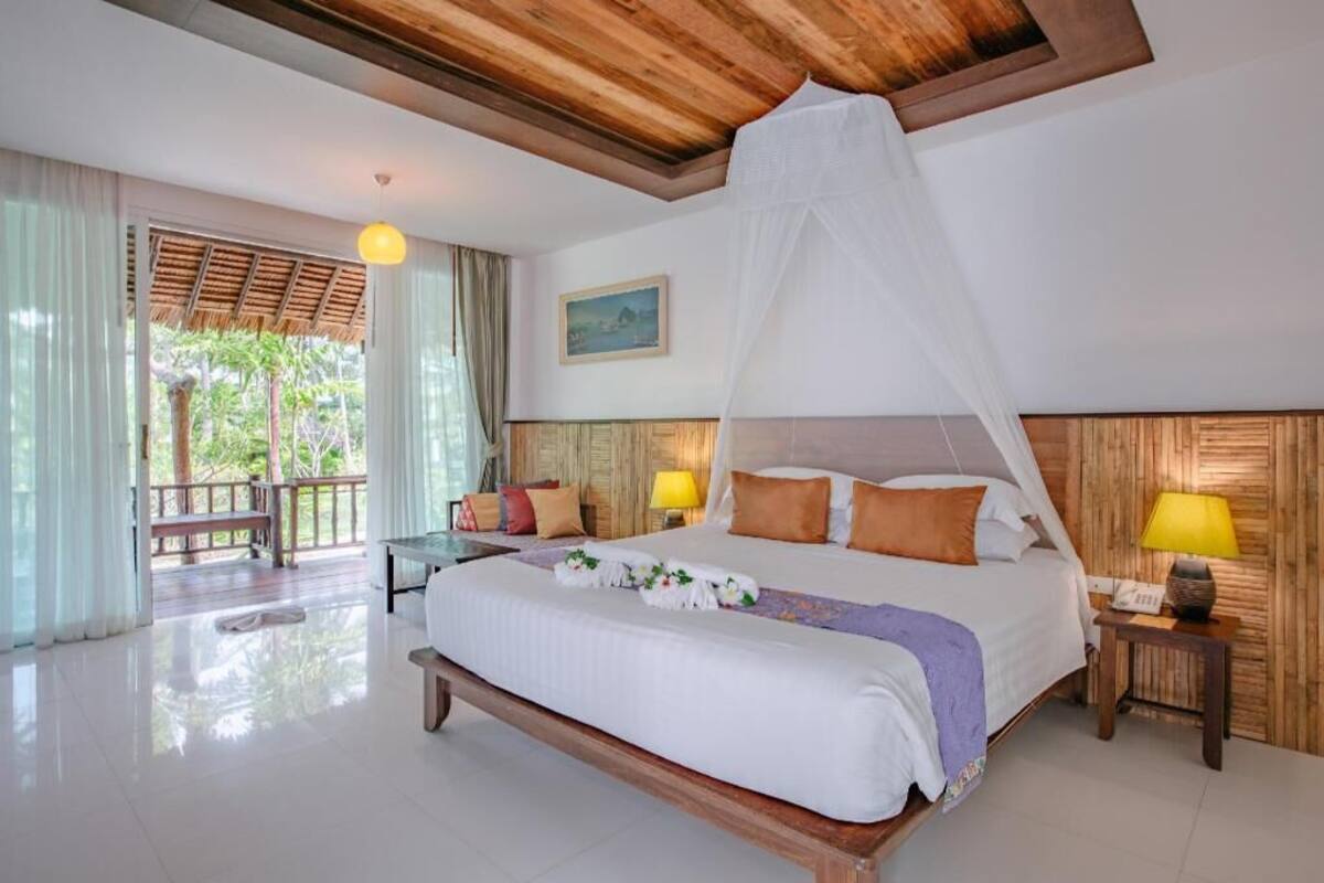 Un dormitorio con cama, mesitas de noche, ventana con cortinas, techo de madera y un cuadro en la pared.
