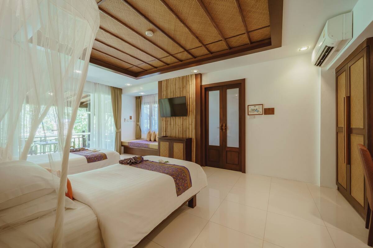 Una habitación de hotel con dos camas, un televisor, un ventanal grande con cortinas y un ventilador de techo.