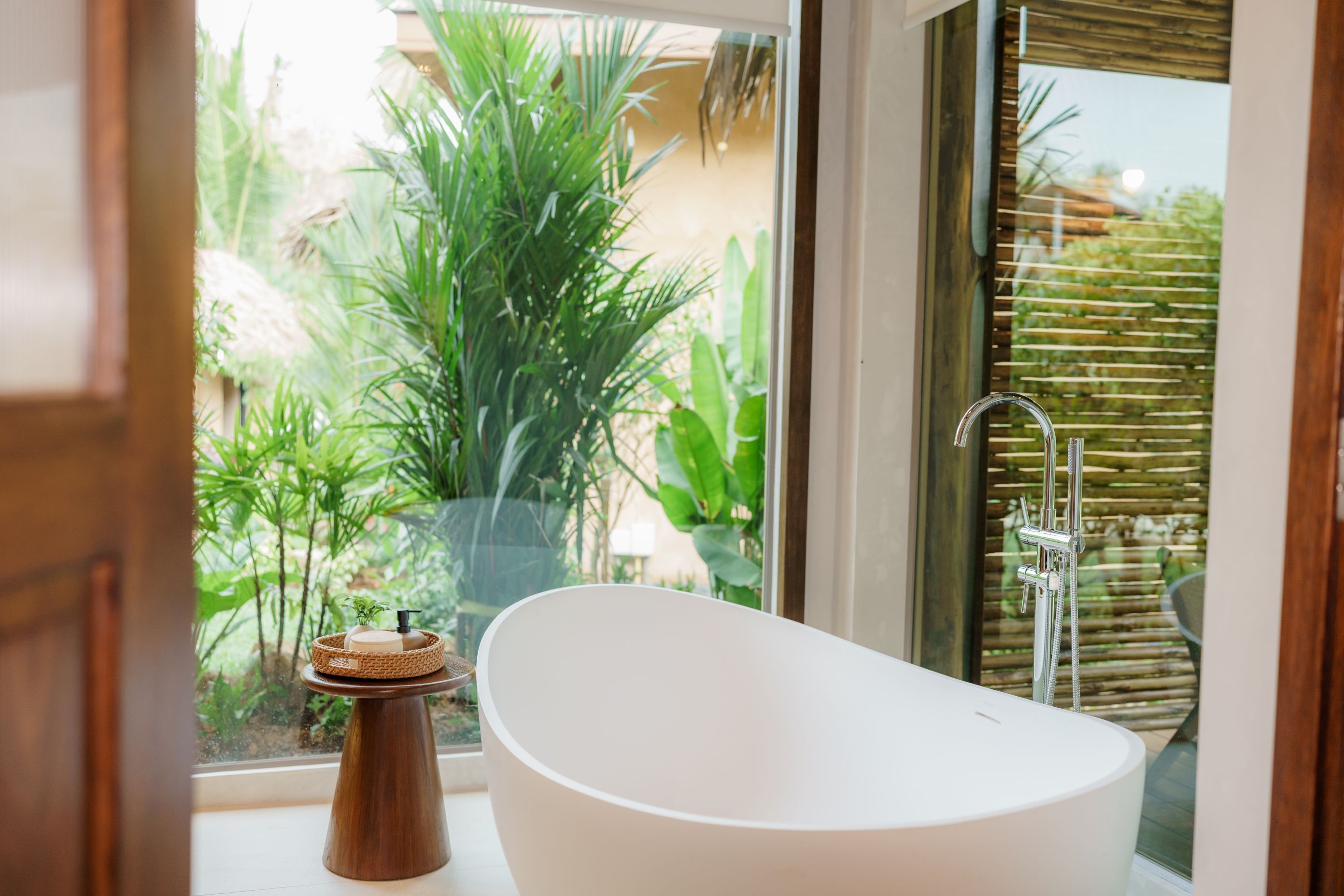Un baño moderno con una bañera independiente, una ventana con vistas a la vegetación y una cerca de bambú.