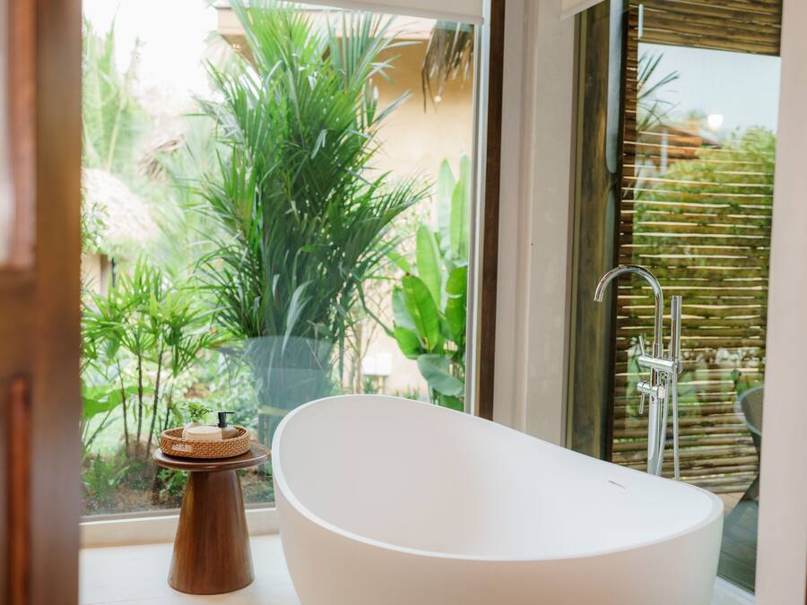 Un baño moderno con una bañera independiente, una ventana con vistas a la vegetación y una cerca de bambú.
