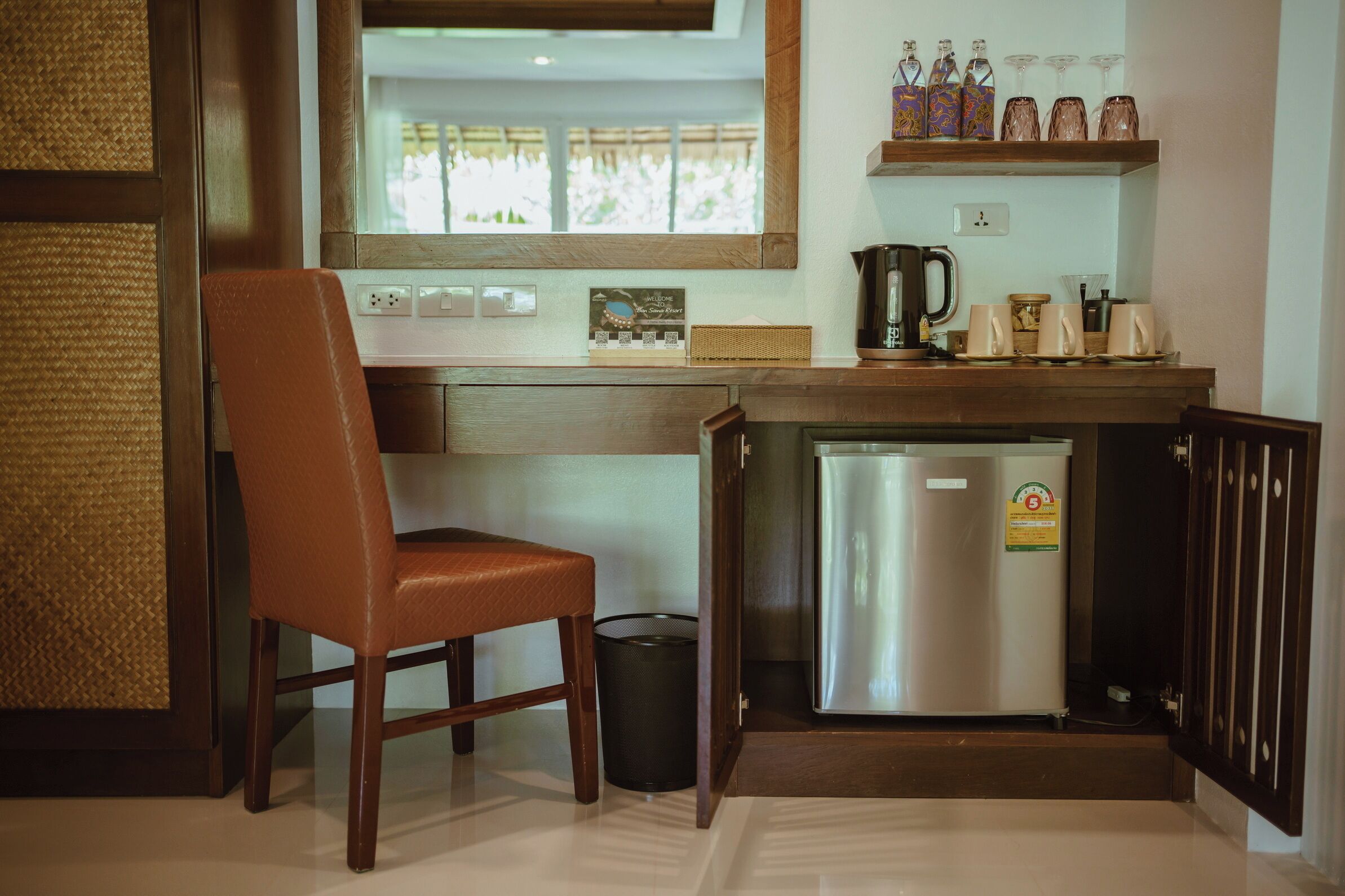 A compact kitchen with a wooden chair, a stainless steel refrigerator, and a coffee maker on the counter.