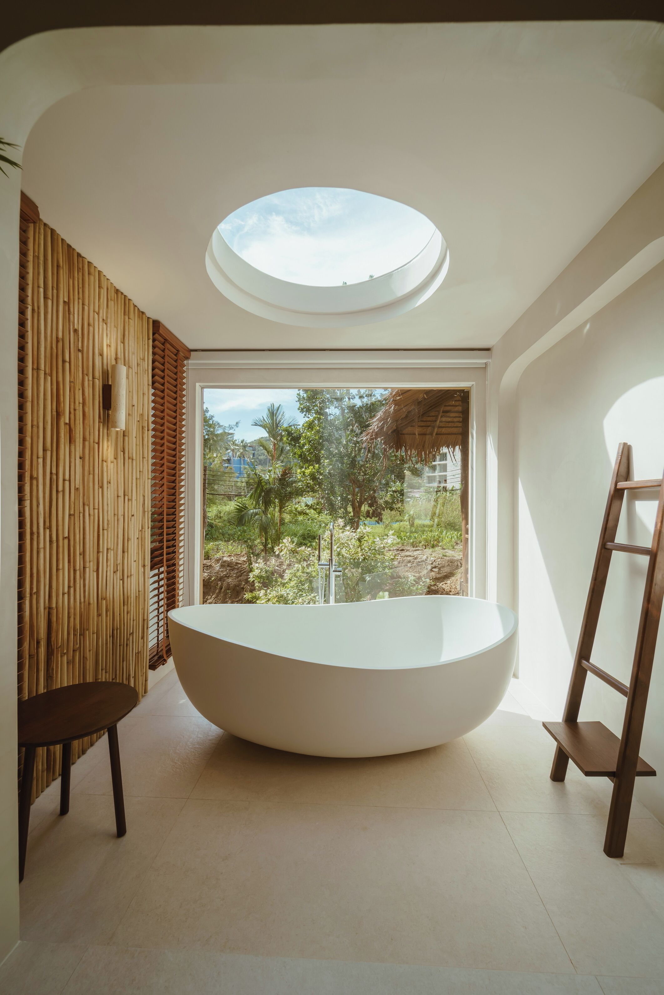 A modern bathroom with a skylight, a freestanding bathtub, and a view of greenery outside.