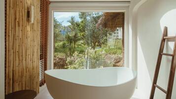 A modern bathroom with a skylight, a freestanding bathtub, and a view of greenery outside.