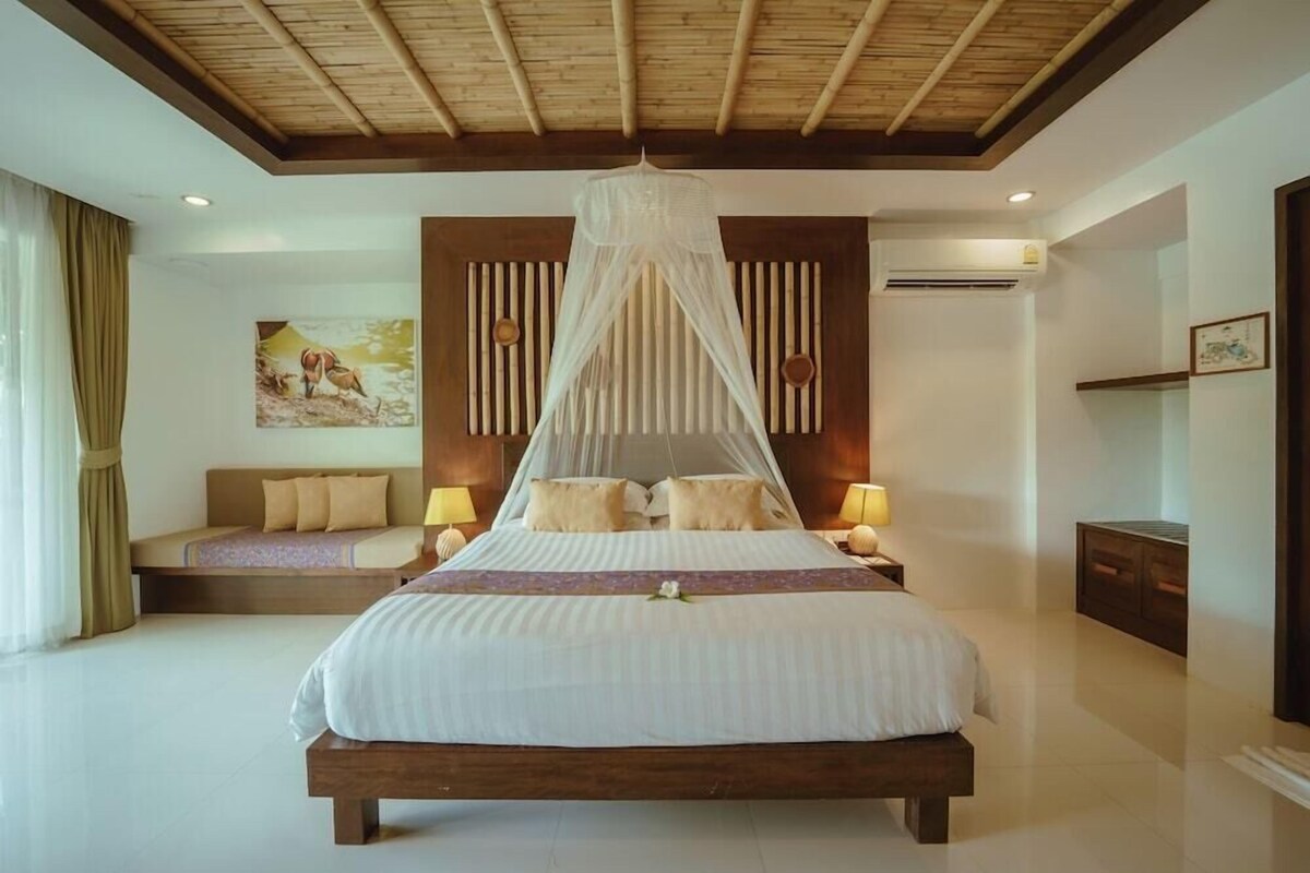 A bedroom with a bed, bedside tables, a canopy bed, a painting on the wall, and an air conditioning unit.