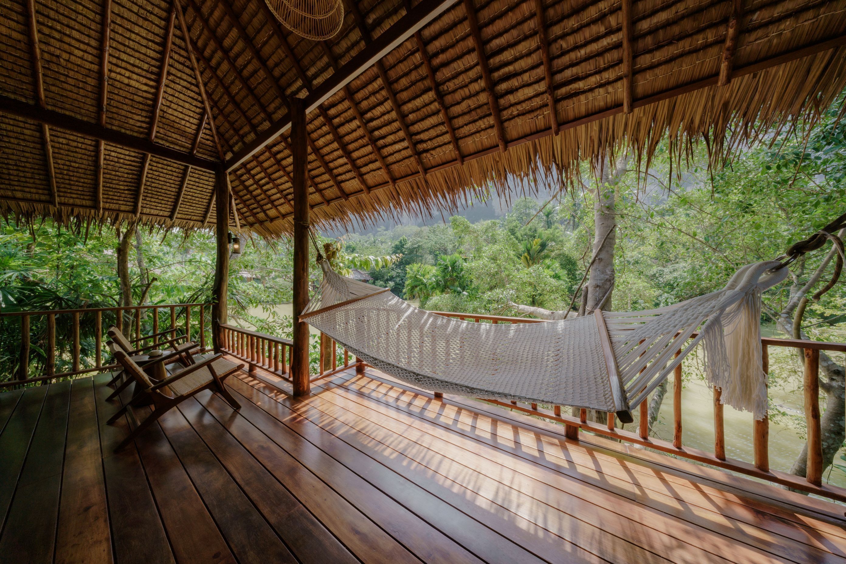 A wooden deck with a hammock and a wooden bench, overlooking a lush green forest.