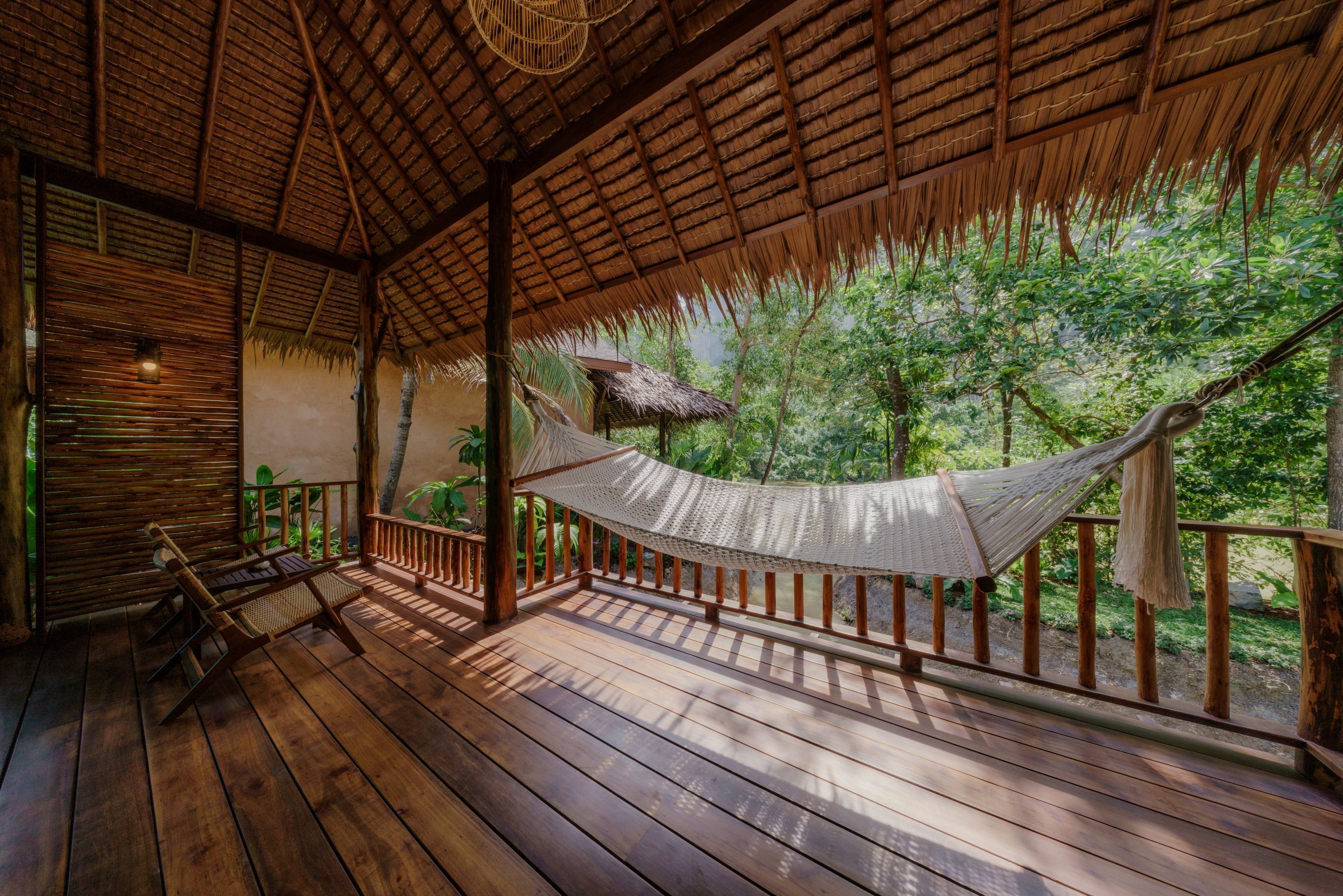 A wooden deck with a hammock, wooden railings, and a thatched roof.