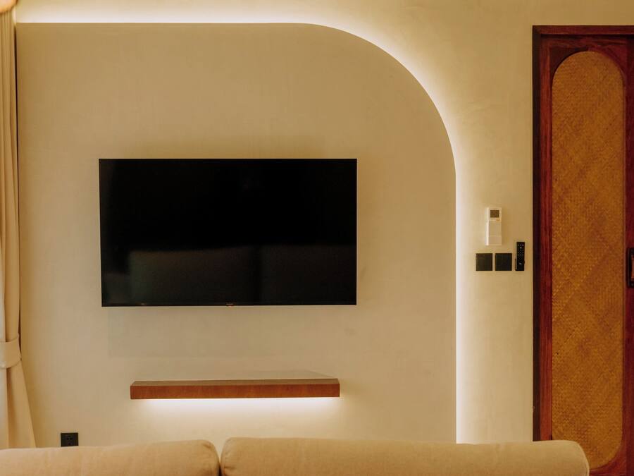 Una sala de estar moderna con un televisor de pantalla plana montado en la pared, un estante de madera debajo y una puerta de madera grande.