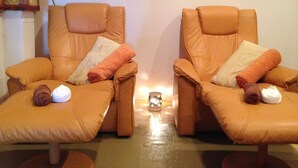 Two leather armchairs with pillows and rolled towels, a small table with a candle, and a window with a curtain. - Aonang Grand Inn (Krabi)