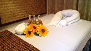 A neatly made bed with a white pillow, a white towel, and a decorative pillow. There are three bottles of water and a bouquet of sunflowers on the bed. - Aonang Grand Inn (Krabi)