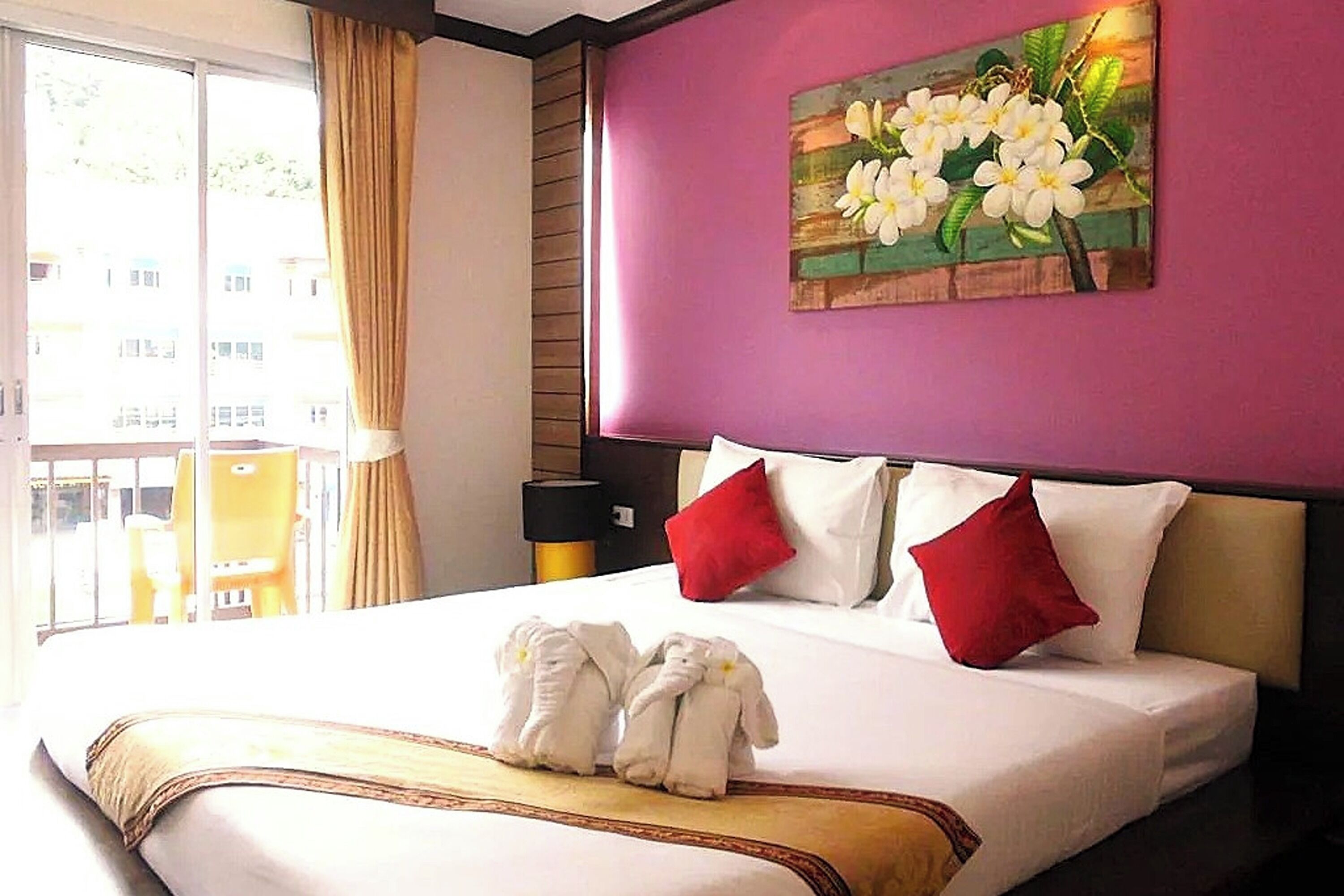 A hotel room with a bed, a painting of flowers on the wall, and a window with curtains.