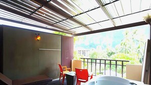Un balcón con un jacuzzi, una zona de estar con sillas y vistas a la vegetación.