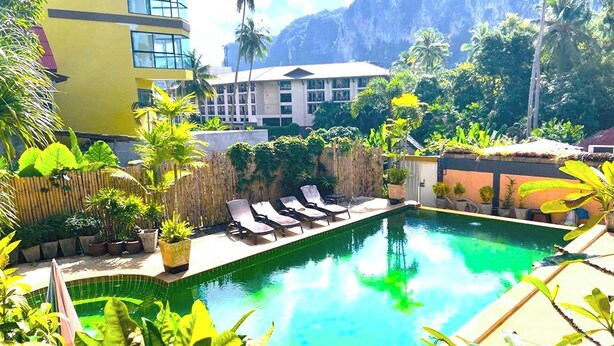 Zona de piscina con sillas de descanso, rodeada de plantas tropicales y con montañas al fondo.