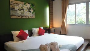 Una cama bien hecha con almohadas blancas y rojas, una pared verde y una ventana con cortinas.