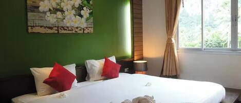 Una cama bien hecha con almohadas blancas y rojas, una pared verde y una ventana con cortinas.