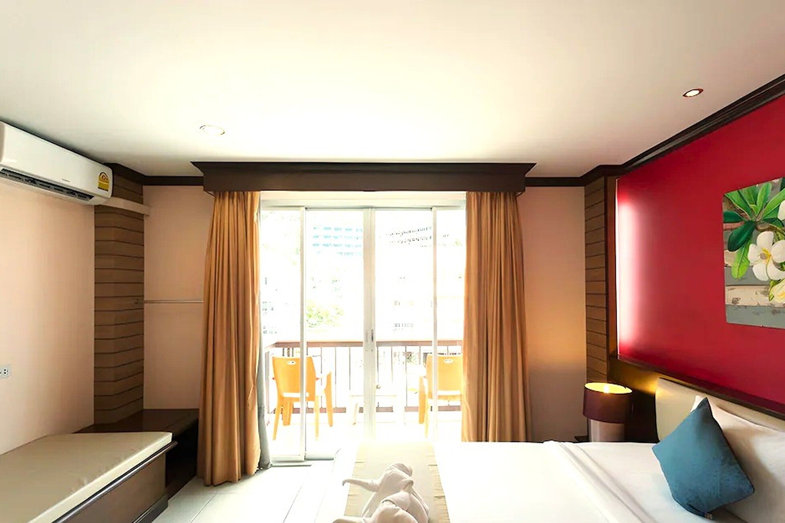 A hotel room with a bed, a desk, a chair, a window with curtains, and a balcony.