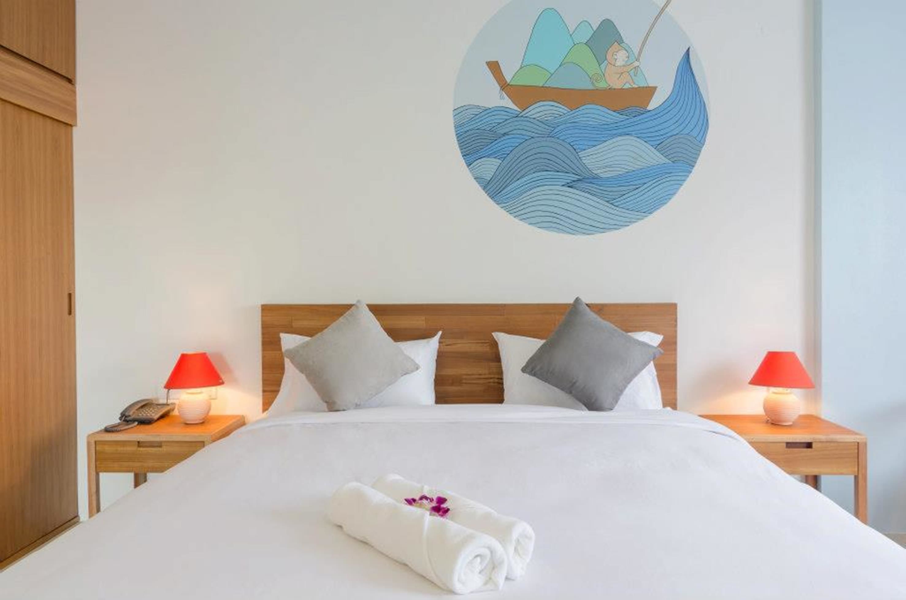 A hotel room with a neatly made bed, two bedside lamps, a wooden headboard, and a wall decoration of a boat on water.